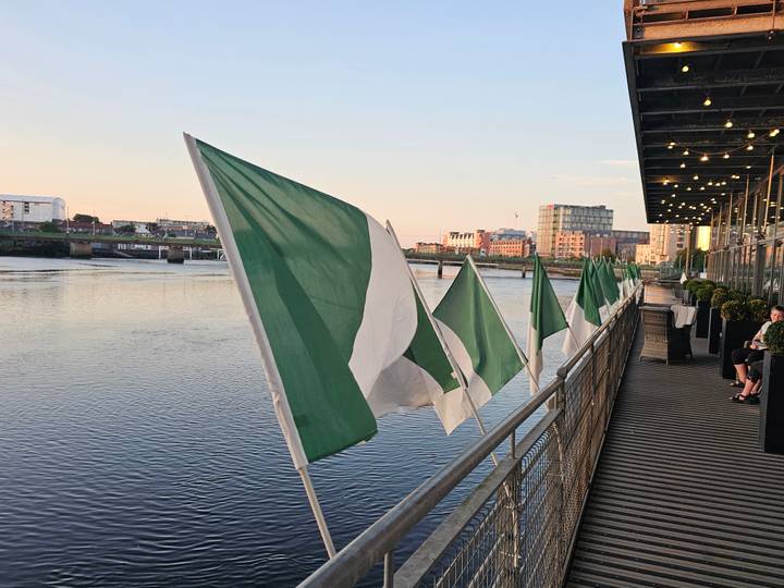 Row of green and white flags fluttering along a riverside promenade at sunset