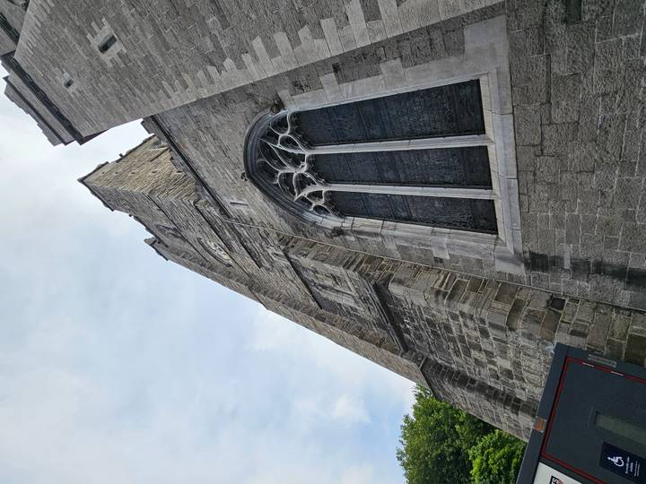 Upward view of a tall stone Gothic church tower with large stained glass window