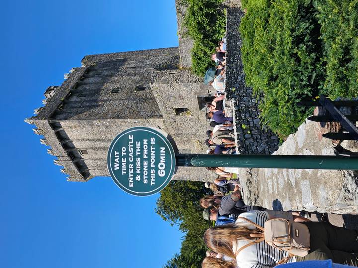 Crowd waiting outside Blarney Castle with a sign noting 60-minute wait time