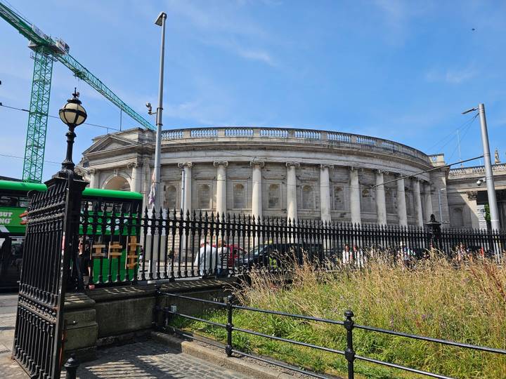Classical colonnaded Bank of Ireland building behind black fence and tram wires