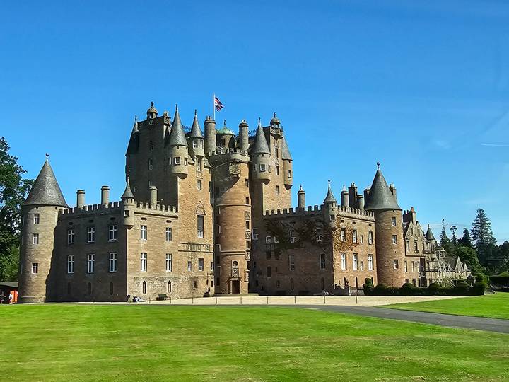 Majestic Glamis Castle set against a blue sky with manicured lawns in front