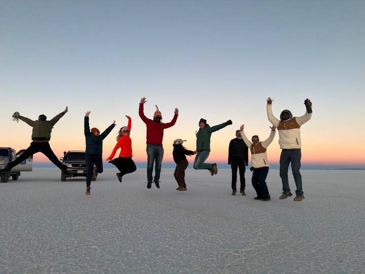 Group of travelers leap joyfully into the air on the vast white expanse of Bolivia’s Uyuni Salt Flat at dawn.