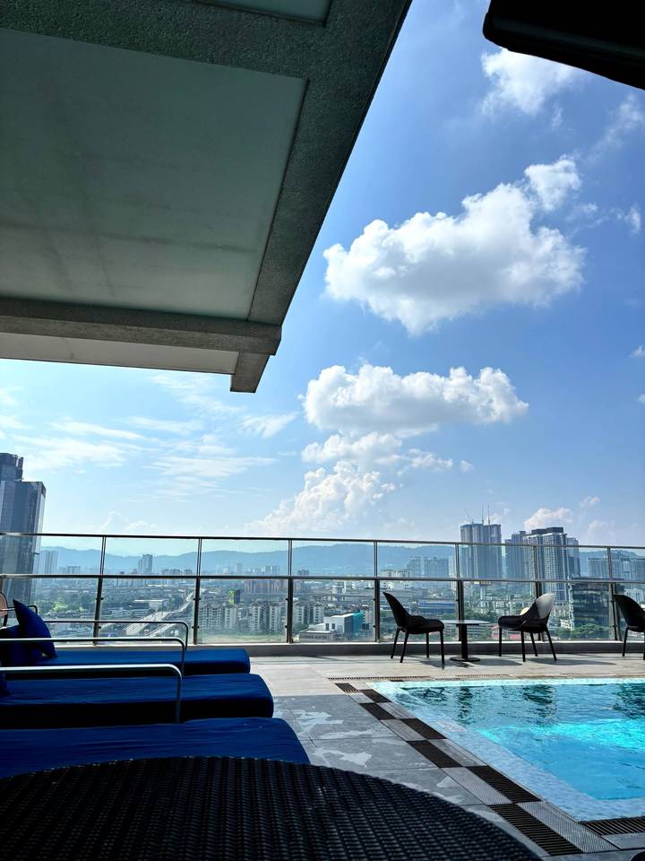 Modern Kuala Lumpur skyline viewed from a hotel rooftop under bright blue sky with scattered clouds