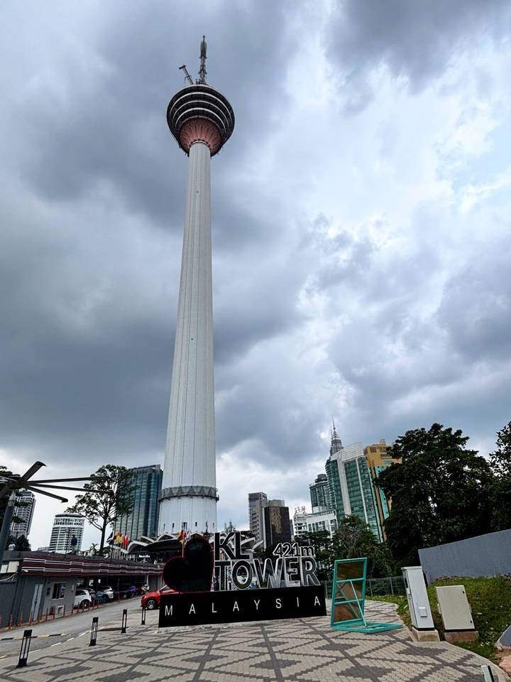 Tall KL Tower standing against a cloudy sky with city buildings in the background