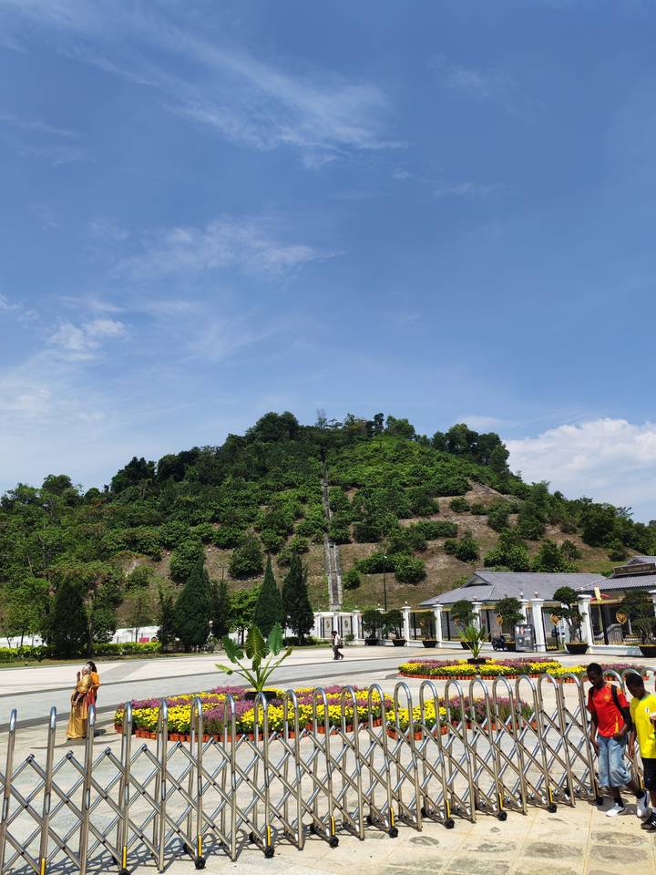 Green terraced hill with long flight of stairs leading to summit under clear blue Kuala Lumpur sky.