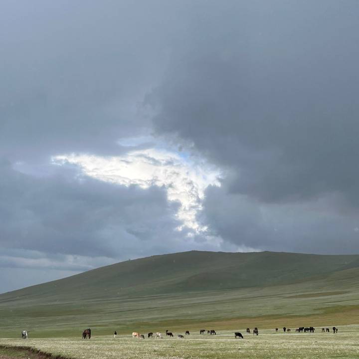 Moody sky with dramatic break in clouds over low green hill.