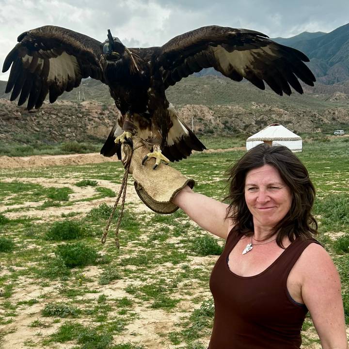 Woman holds a golden eagle on gloved arm with yurt and mountains in background.