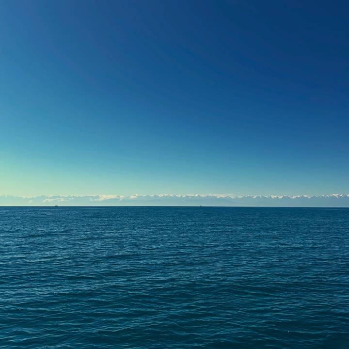 Vast blue lake stretching to the horizon with distant snow-covered mountain range.