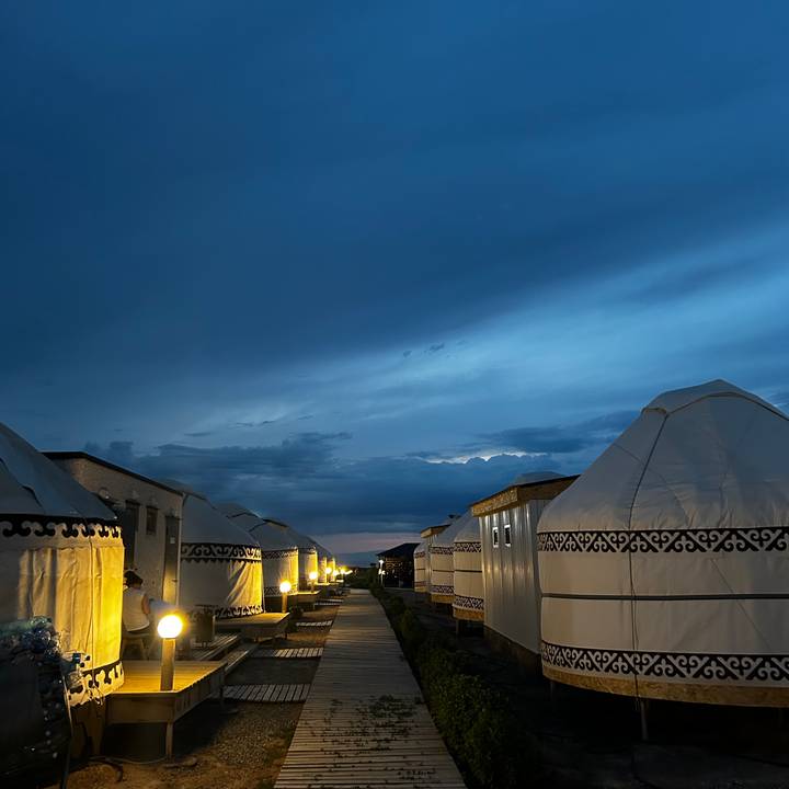 Row of illuminated yurts at twilight under a deep blue evening sky.