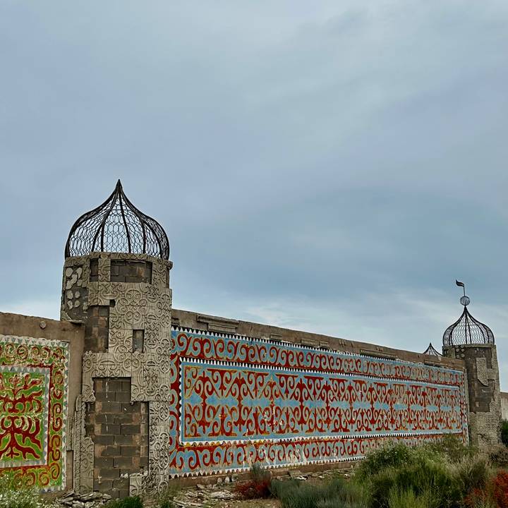 Decorative wall with colorful patterns and wrought-iron turrets under a grey sky.