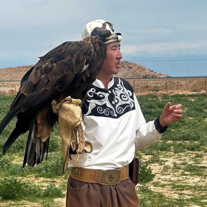 Eagle hunter wearing traditional clothing holds a golden eagle while explaining to visitors.