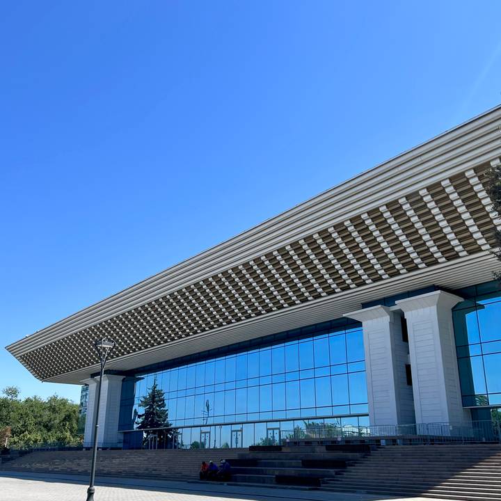 Modern glass-clad building with striking patterned roof lines against cloudless sky.