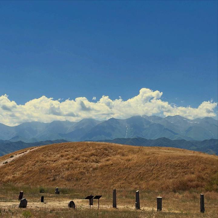 Golden grassy ridge with vast mountain range and fluffy clouds beyond.