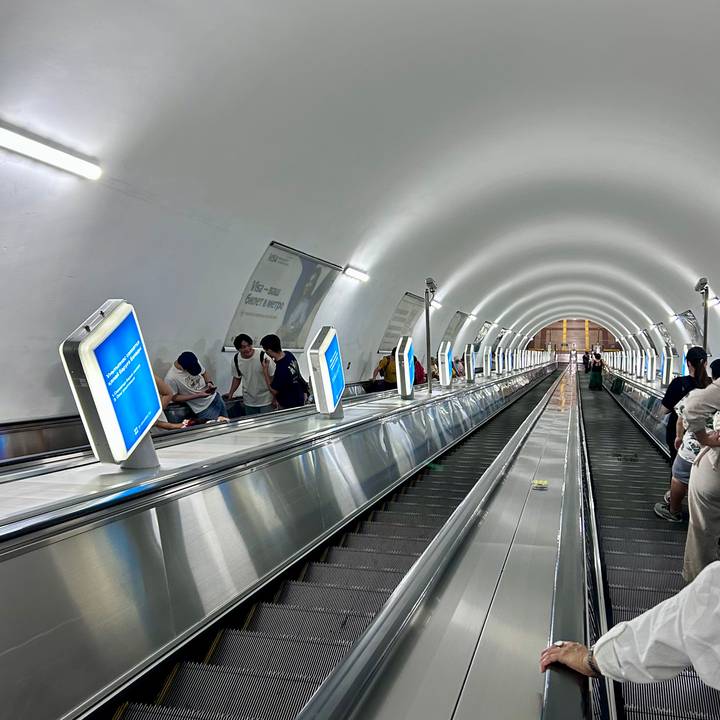 Long, steep underground metro escalator tunnel with passengers riding up and down.