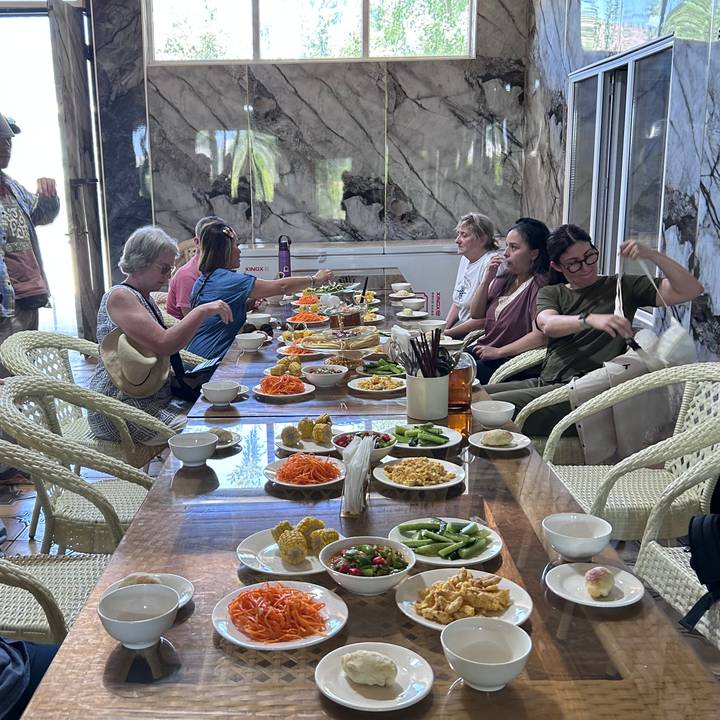 Tour group seated around a wooden table enjoying a spread of salads and local dishes.