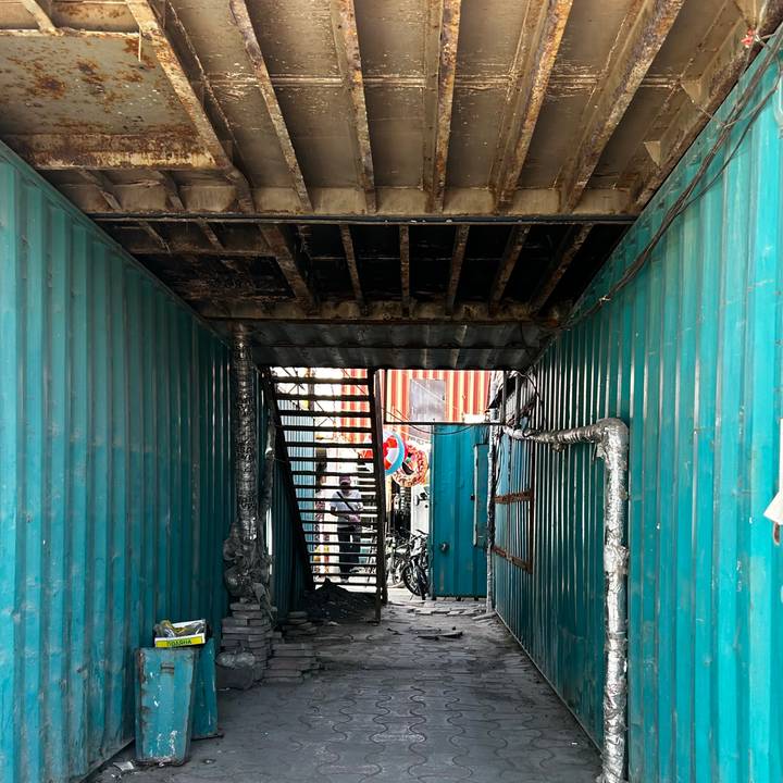 Narrow industrial corridor made from teal shipping containers leading to a staircase.