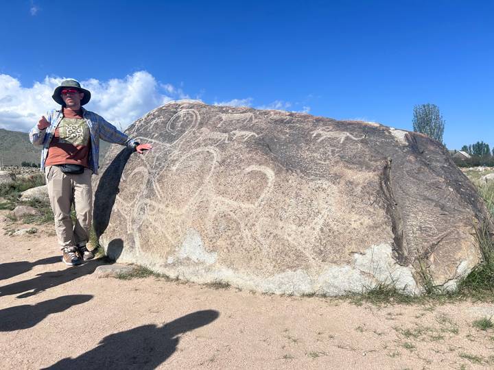 Guide explaining ancient petroglyphs etched on a large boulder under blue sky