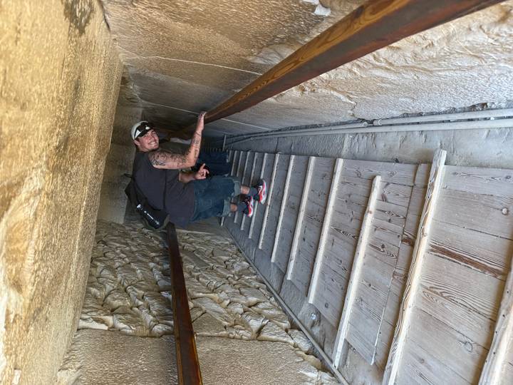 Visitor climbs a steep wooden staircase inside the narrow passage of a pyramid.