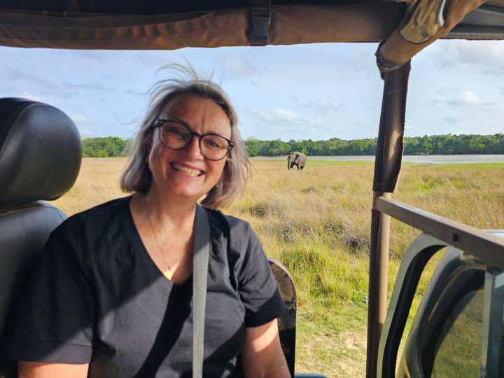 Traveller in safari jeep smiling with a wild elephant roaming grassy plain behind