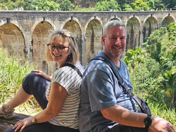 Couple seated back-to-back near the famous Nine-Arch Bridge surrounded by jungle