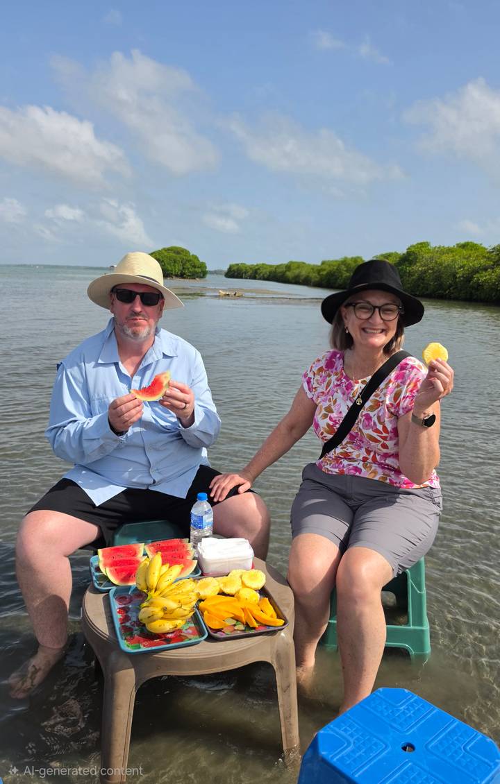 Smiling couple seated on a boat enjoying fresh fruit slices with mangroves in the background.