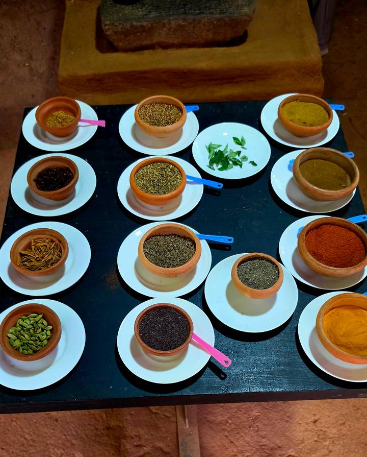 Overhead arrangement of clay bowls filled with assorted spices on white plates during a cooking class.