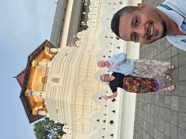 Tourists posing for a selfie in front of the white Temple of the Tooth complex at dusk.