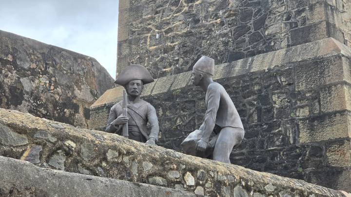 Weathered stone sculptures of colonial soldiers positioned on the ramparts of a historic fort.