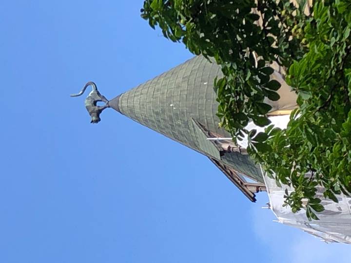 Iconic cat statue perched atop the pointed turret roof of Riga’s Cat House against a clear blue sky.