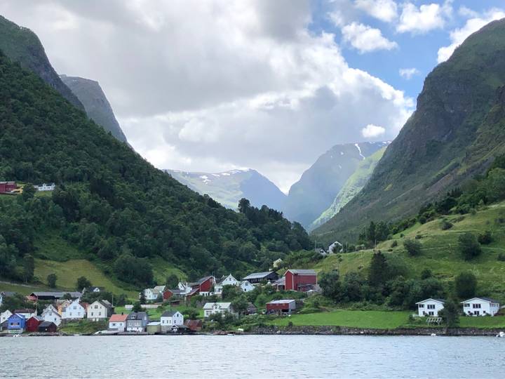Picturesque Norwegian fjord village surrounded by verdant mountains and dramatic cloudy sky.