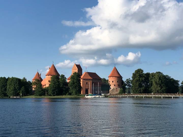 Red-roofed Trakai Island Castle reflected in a tranquil lake beneath a blue sky with puffy clouds.