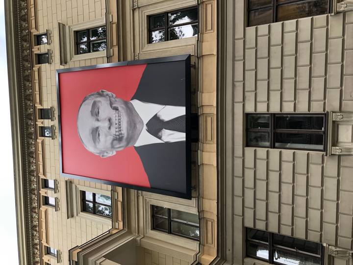 City building façade featuring a large provocative billboard of a political figure with skull overlay.
