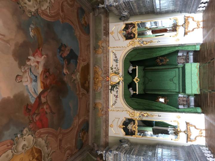 Lavish baroque palace bedroom with an emerald green throne-like bed and painted ceiling frescos.