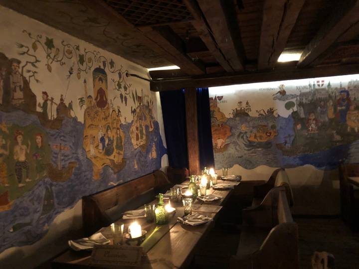 Dimly lit medieval-themed restaurant interior with long wooden tables, candles and painted story murals.