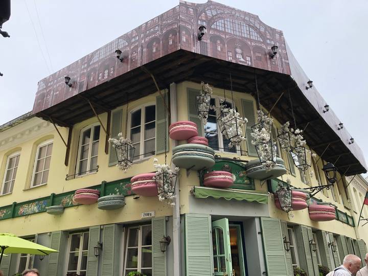 Quirky corner café building decorated with oversized pastel macaron sculptures and partially covered by renovation sheeting.