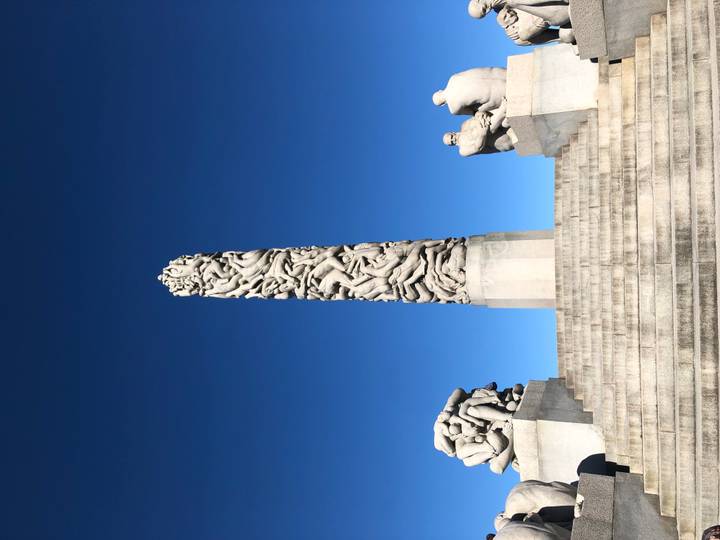 Stone monolith sculpture surrounded by human figures on stairs against a clear deep-blue sky.
