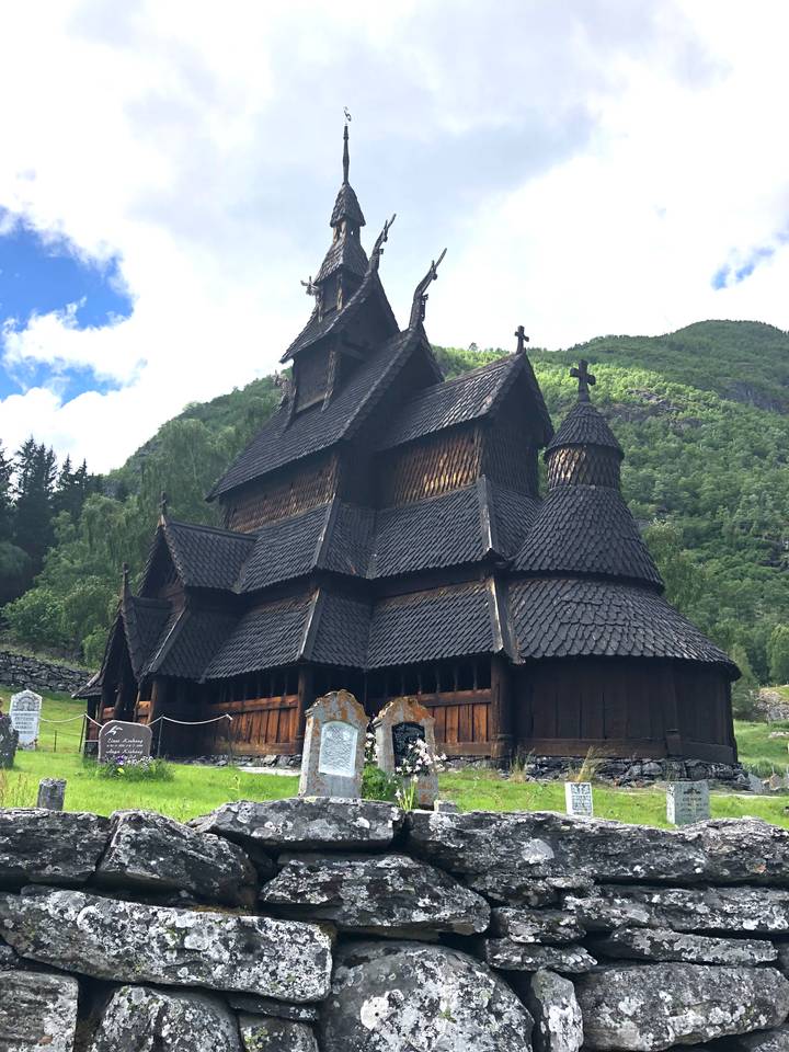 Dark wooden stave church with steep multi-tiered roof framed by forested hills.