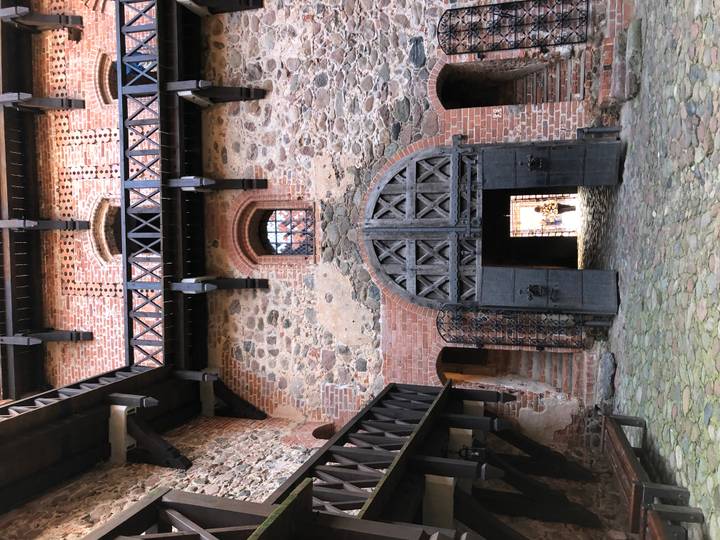 Interior courtyard of a red-brick medieval castle with a large arched wooden door; a single person seen through doorway.