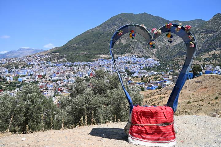 Heart-shaped metal sculpture overlooks the blue and white town of Chefchaouen nestled below green mountains.