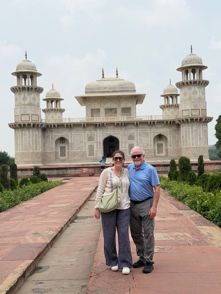 Smiling duo posing in front of ornate white marble tomb with intricate inlay work and minarets.