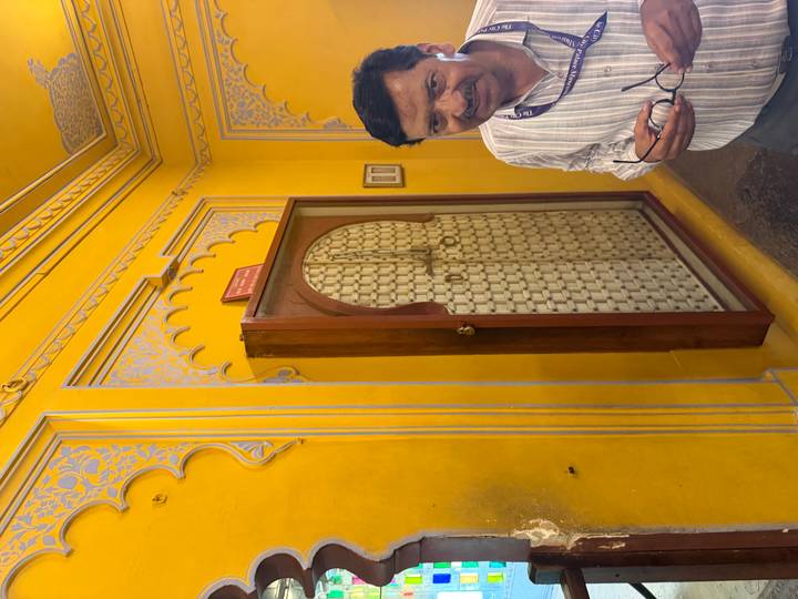 Bright yellow intricately painted palace wall with arched niche and a visitor holding glasses.