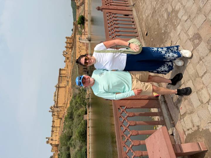 Travelers posing on a bridge with the massive yellow Amber Fort rising behind them.