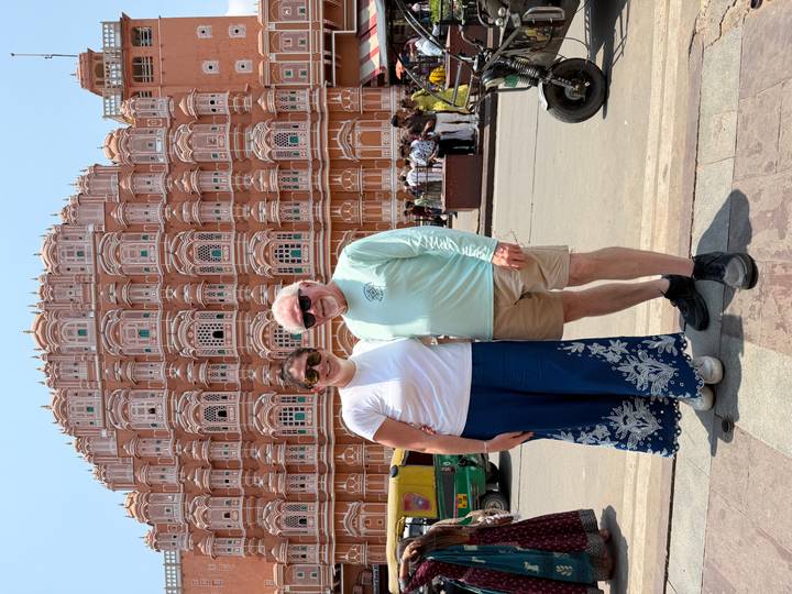 Couple standing in front of the ornate pink facade of Hawa Mahal on a sunny day.