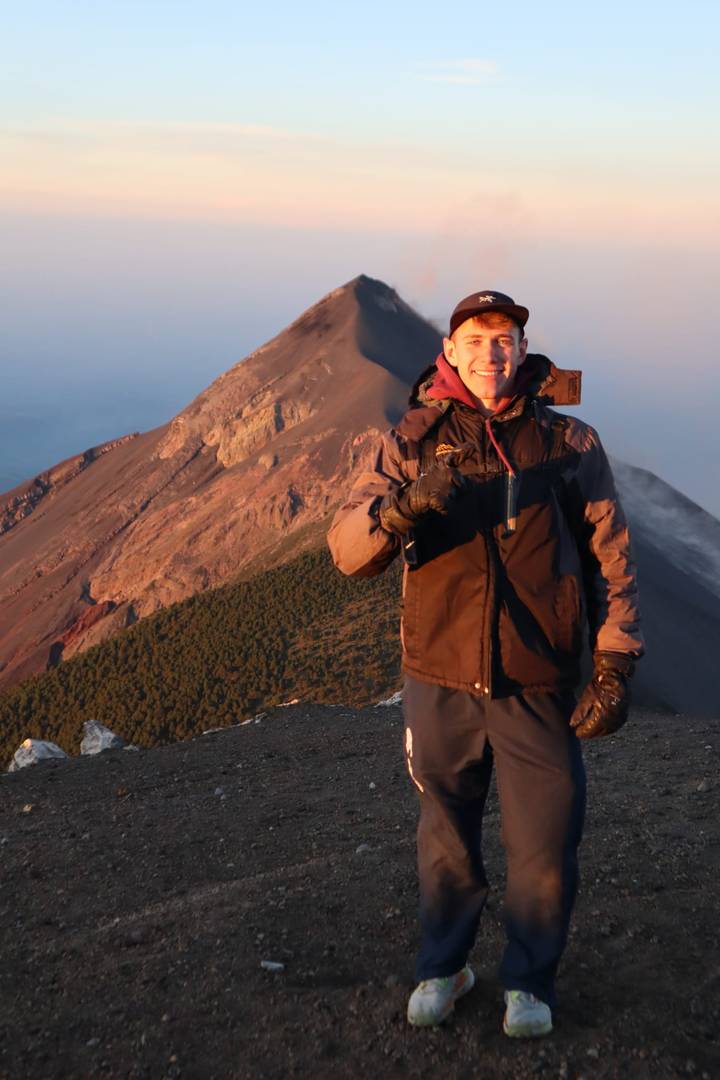 Solo hiker giving thumbs up on volcanic ridge with dramatic sunrise light on crater