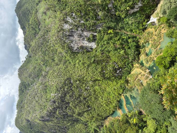 Lush green mountains with turquoise stepped pools and a river flowing through a deep jungle valley.