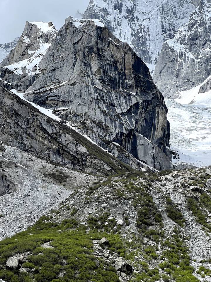 Textured close-up of steep granite cliff faces with patches of snow and greenery.