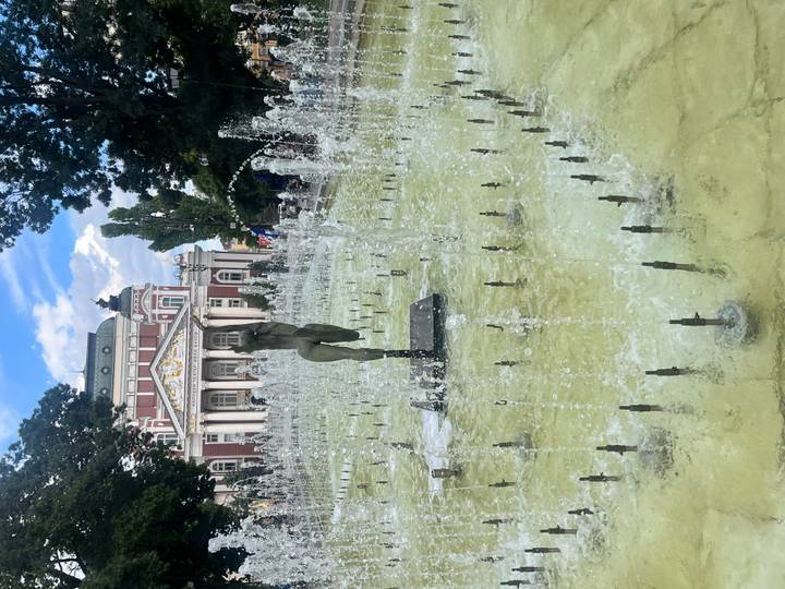 Dancing fountain spraying water jets in front of Sofia's ornate National Theatre on a bright afternoon.