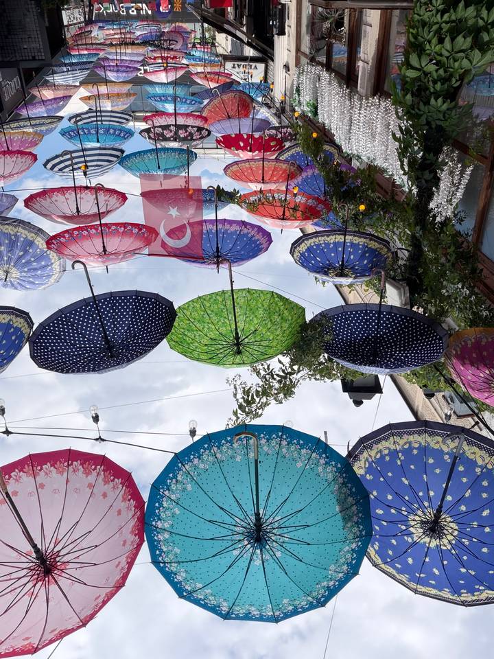 A canopy of colorful patterned umbrellas strung above a narrow street with a small Turkish flag banner.