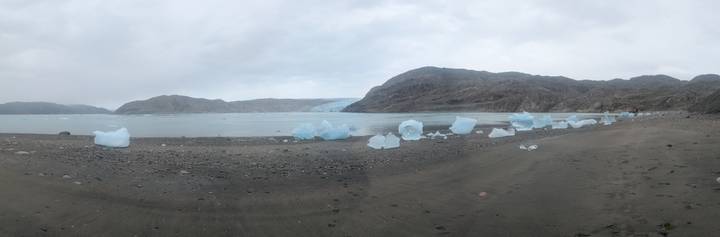 Blue icebergs lie scattered on a black sand beach below a distant glacier tongue.