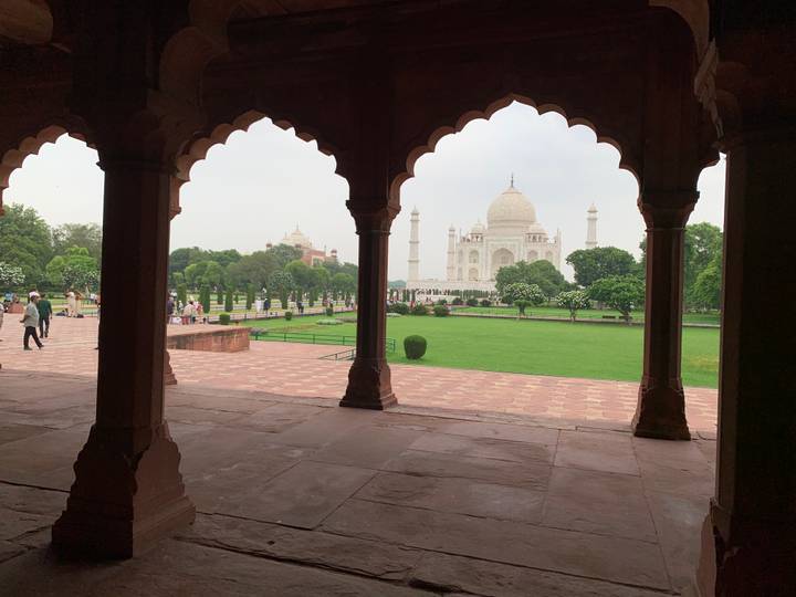 View of the Taj Mahal framed by ornate arched columns of a red-sandstone pavilion